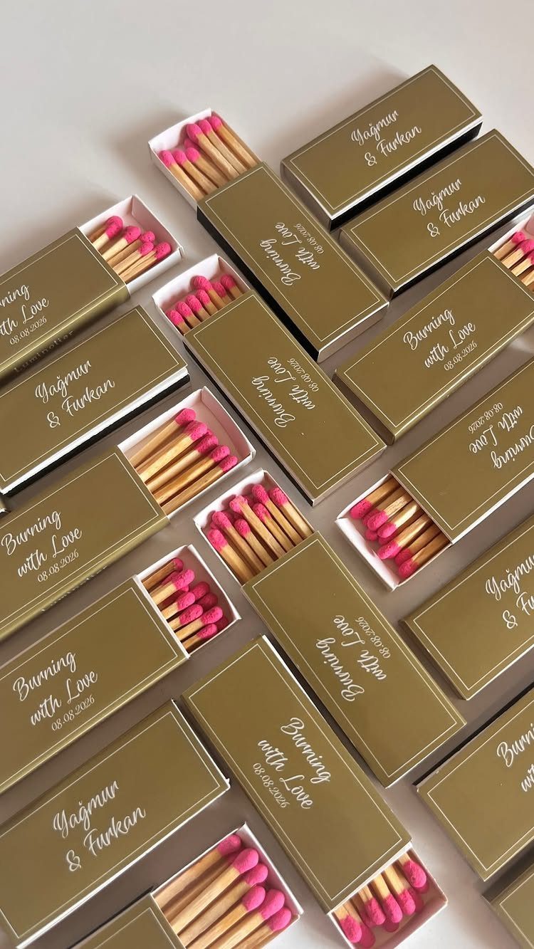Gold customized matchboxes with pink tipped matches and white cursive wedding text.