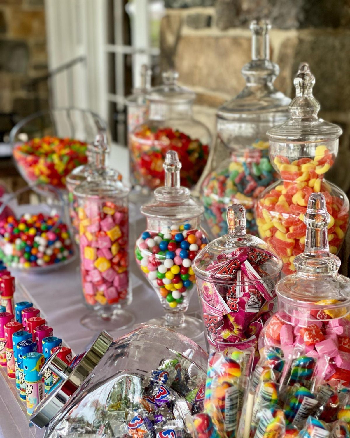 Colorful candies in glass jars arranged on a white table for a buffet.