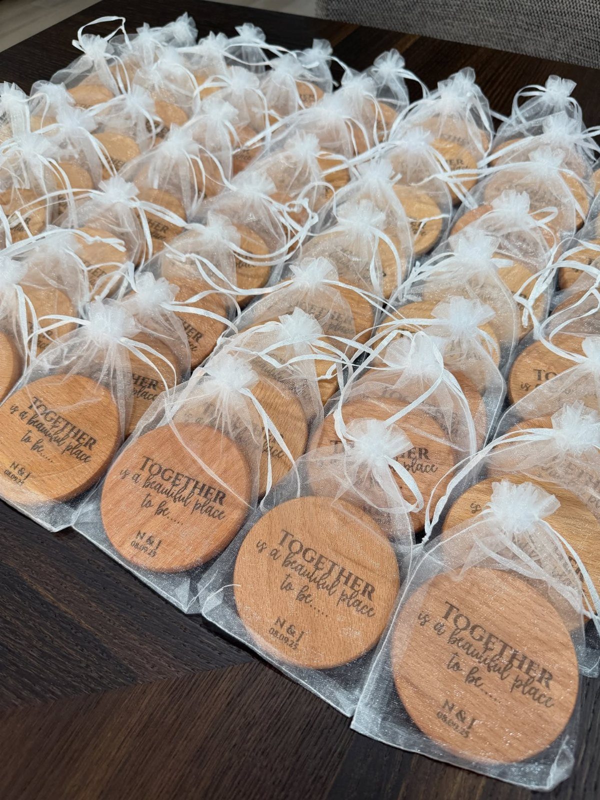 Engraved wooden coasters in white organza bags arranged on a dark wooden table.