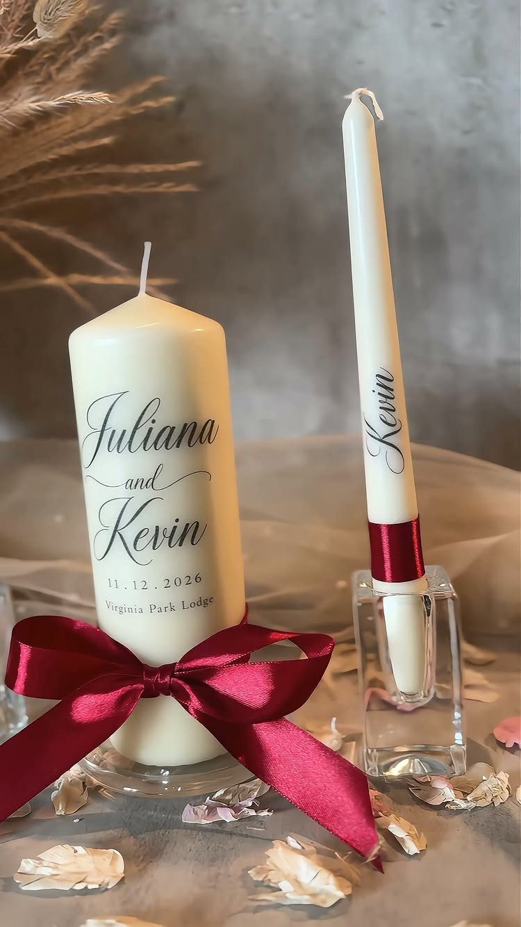 White personalized wedding candles with names and a red satin bow on petals.