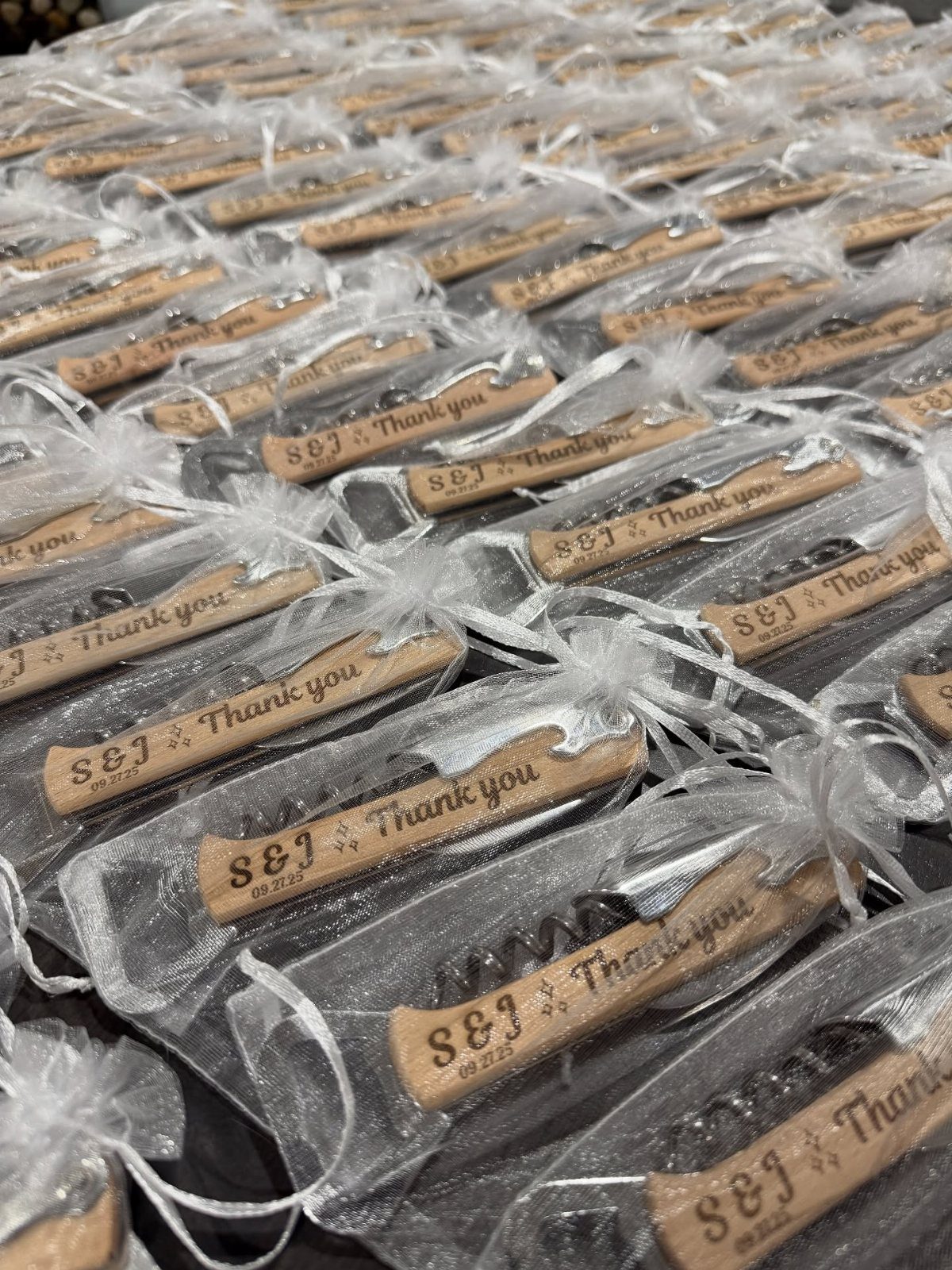 Personalized wooden wine bottle stoppers in white organza bags arranged in rows.
