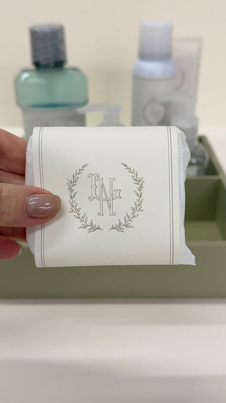 White monogrammed packet held in front of a tray of bathroom toiletries.