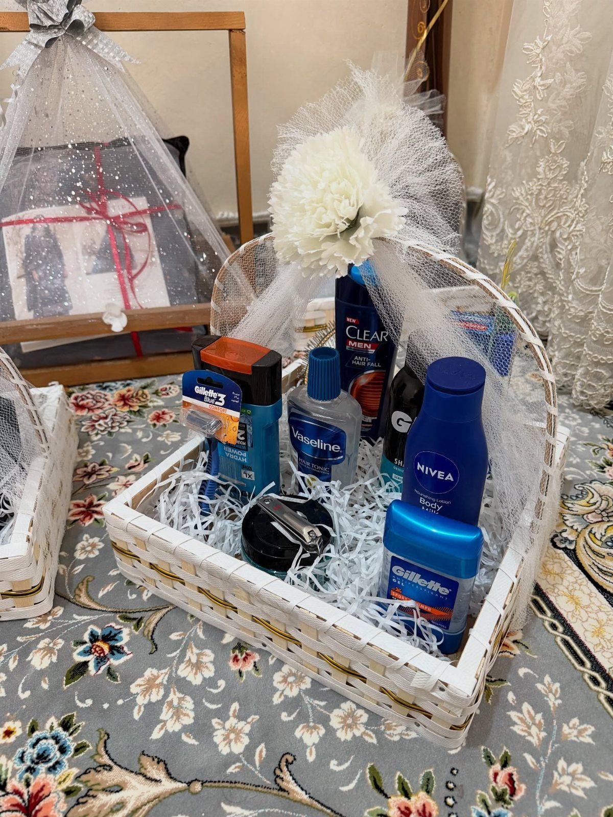 White wicker basket with men's toiletries and a white tulle bow on floral fabric.