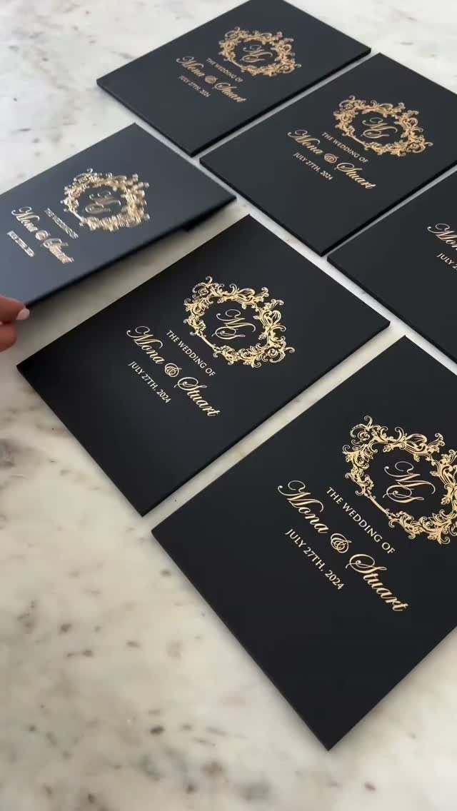 Black wedding invitations with gold foil calligraphy and crests on marble surface