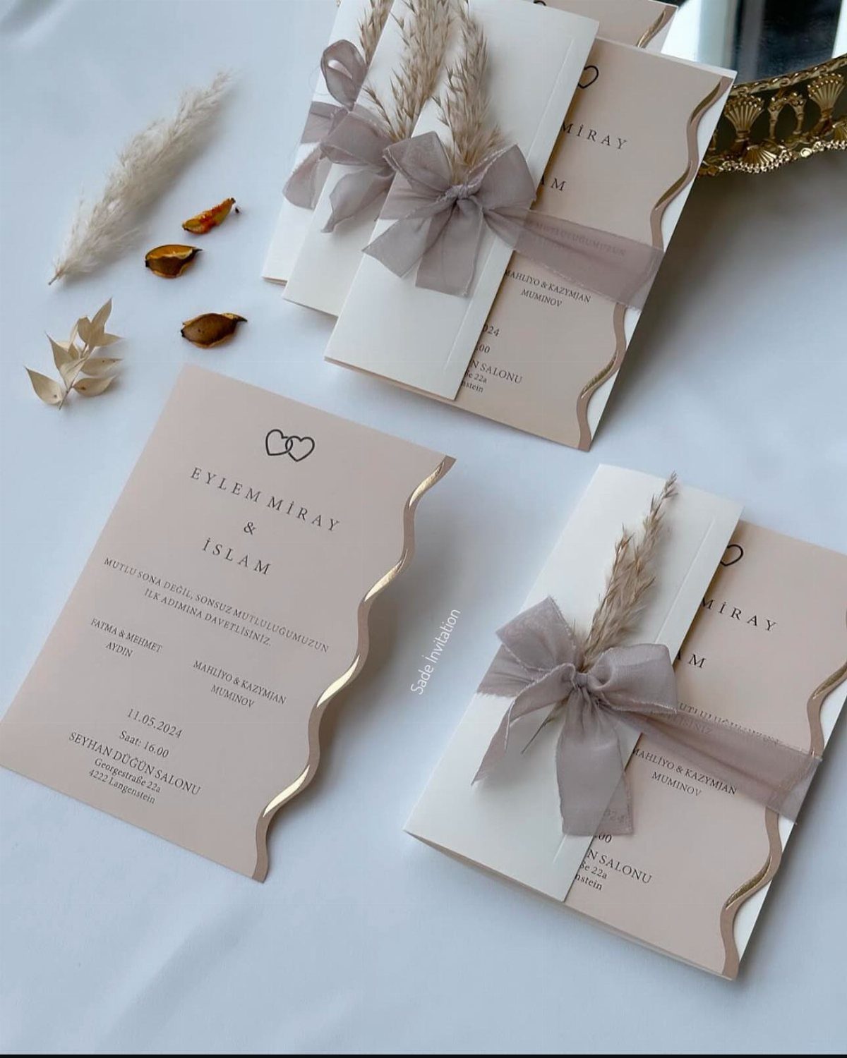 Blush and white wedding invitations with minimal typography, grey ribbons, and dried grass.