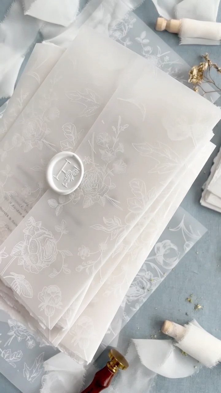 Translucent vellum wedding invitations with floral patterns and a white wax seal.