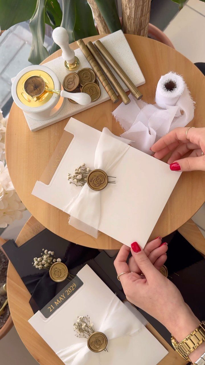 White wedding invitation with a gold wax seal and sheer white ribbon tie.