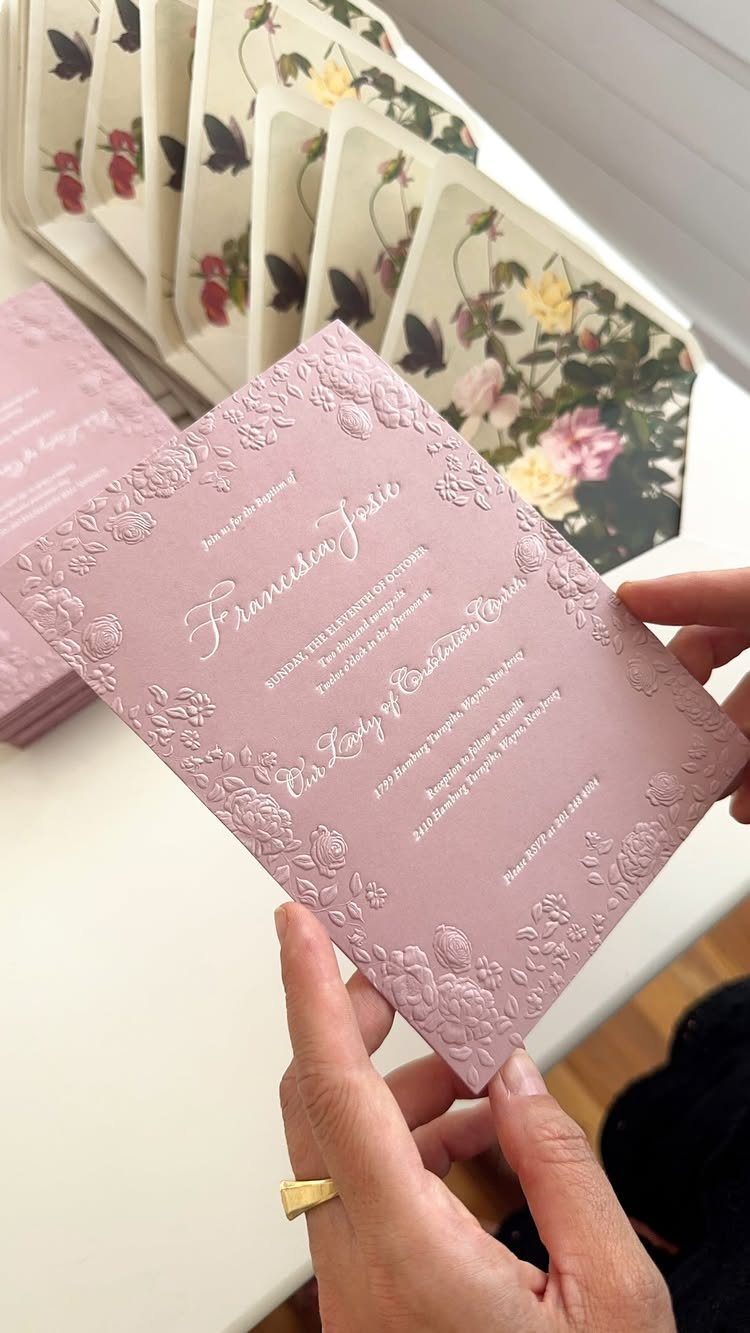Mauve embossed wedding invitation with white calligraphy held by two hands.
