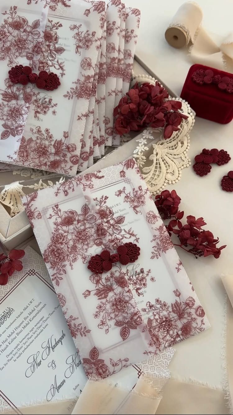 White wedding invitations with red floral patterns and red wax seals on white surface