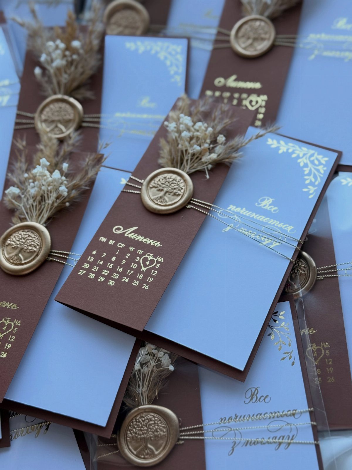 Elegant wedding invitations with gold wax seals, dried flowers, and blue and brown paper.
