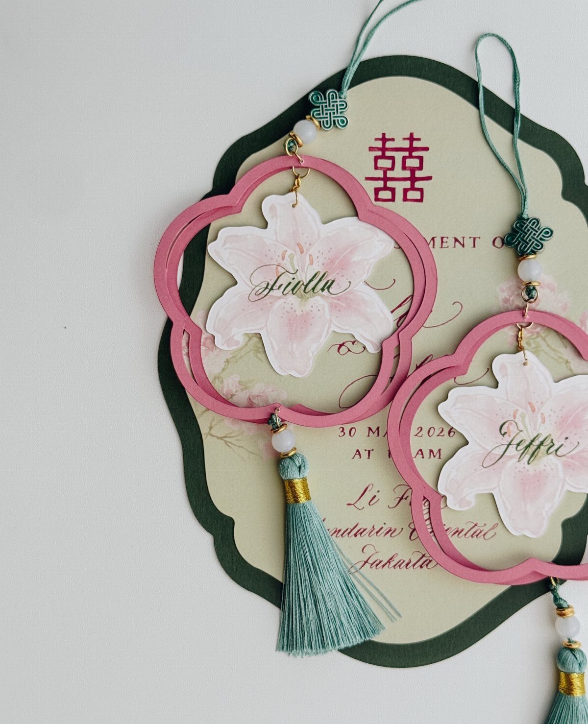 Ornate wedding invitation with pink floral frames, teal tassels, and elegant calligraphy.