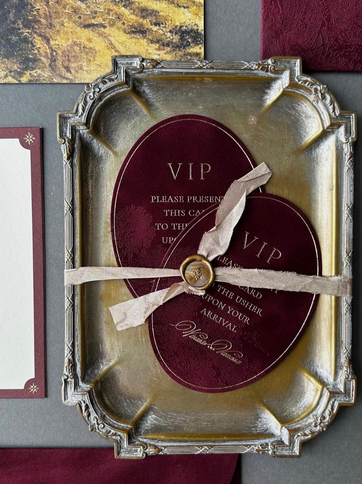 Burgundy velvet VIP invitation cards tied with a ribbon on an ornate tray