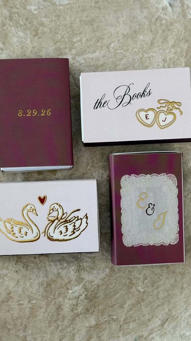 Four small book-shaped favor boxes in burgundy and white with gold wedding details.