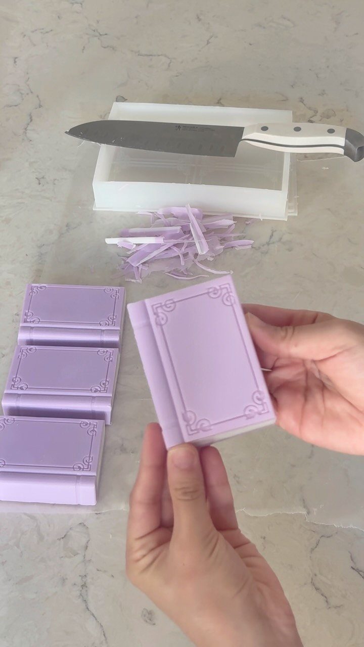 Light purple book-shaped soaps on a marble surface with a white gift box.