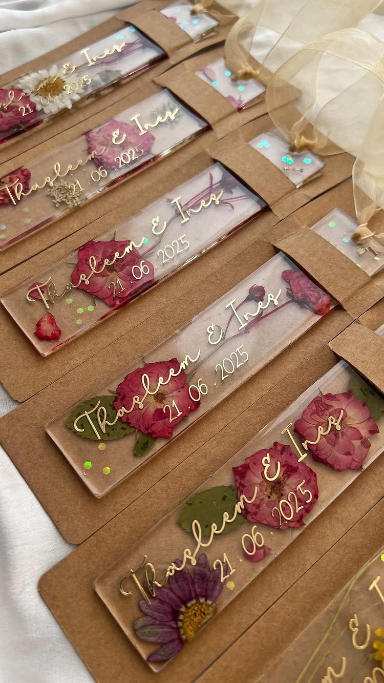 Clear resin bookmarks with pressed flowers and gold personalized text on cardboard backing.
