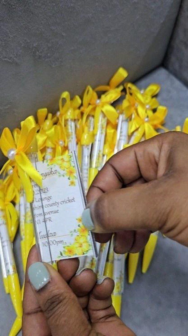Yellow and white pens tied with yellow ribbons and pearls next to a card.