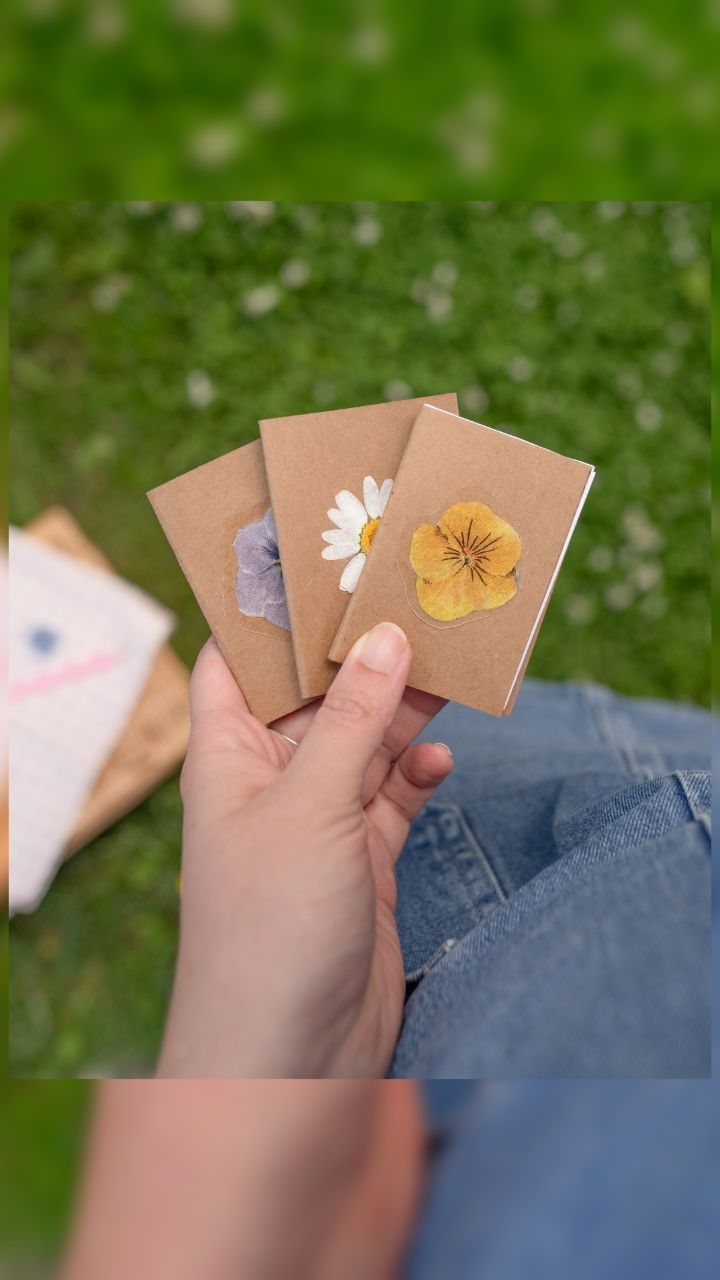 Three mini brown kraft notebooks with pressed flowers held against a green background