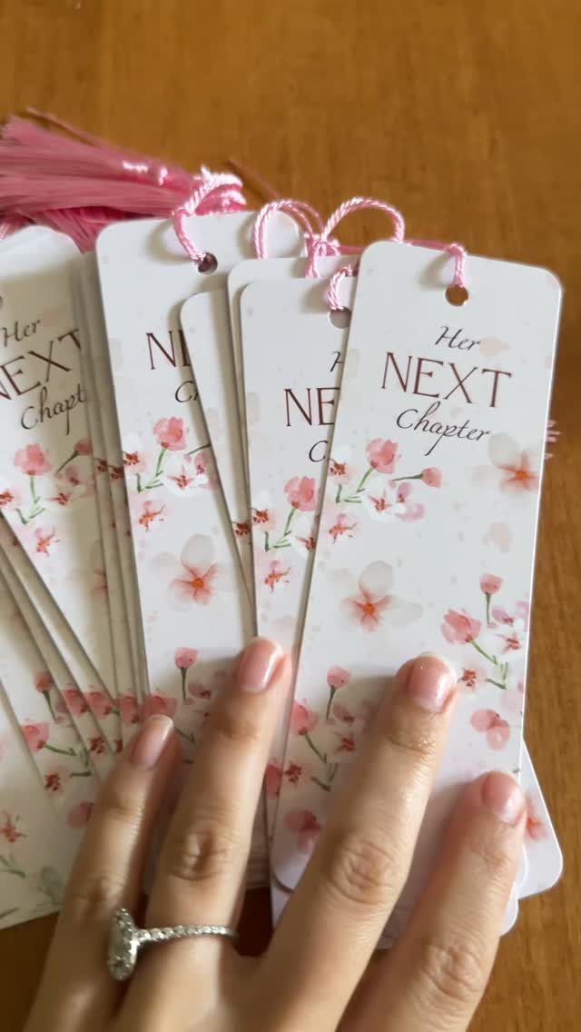White bookmarks with pink flowers and 'Her Next Chapter' text held by hand.