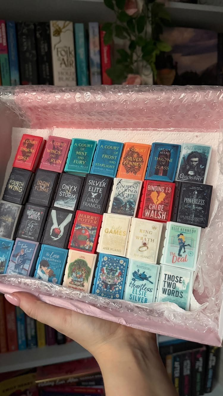 Miniature book replicas arranged in a pink box held by a hand.