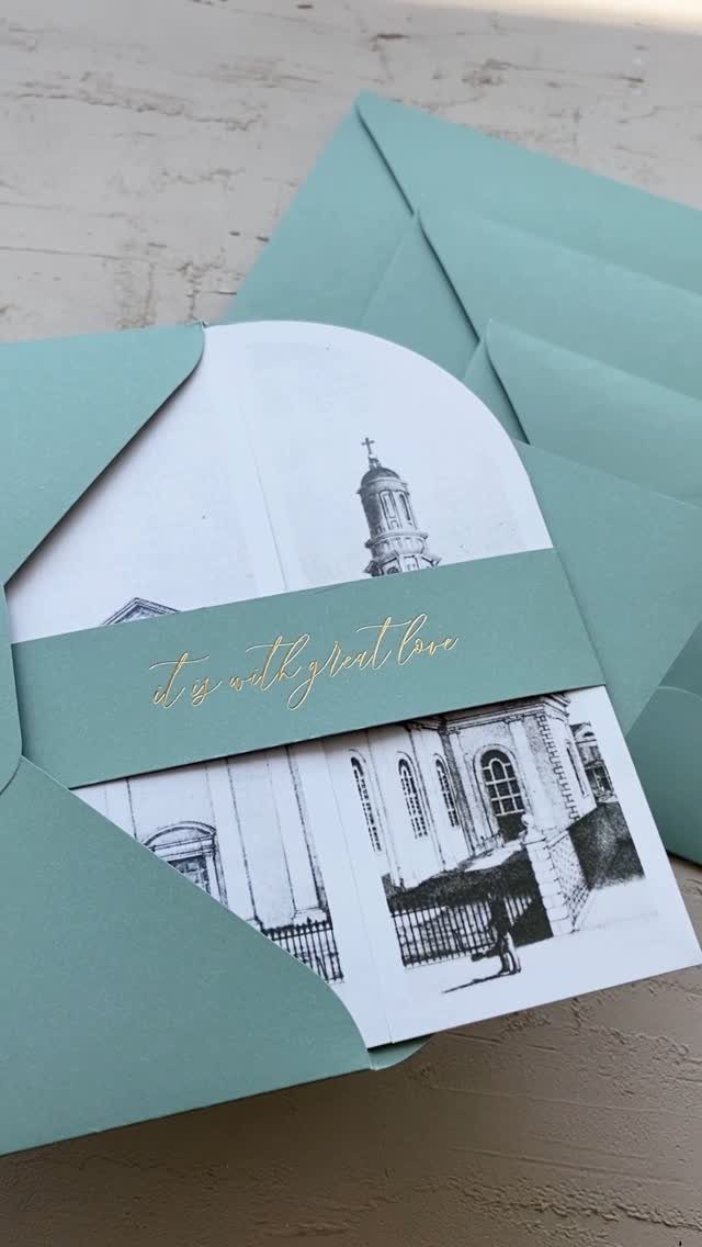 White wedding invitation with church sketch, light blue band, and gold cursive lettering.