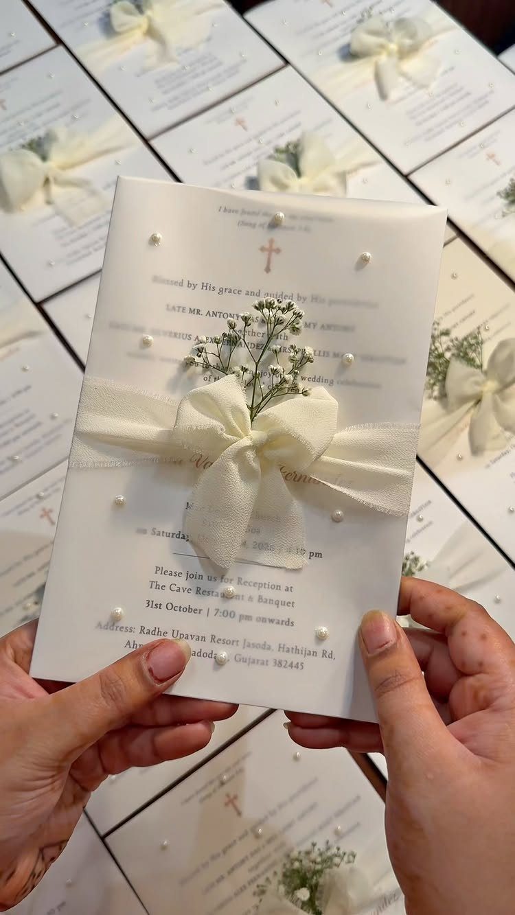 White wedding invitation with a cross, ribbon bow, and baby's breath flowers.