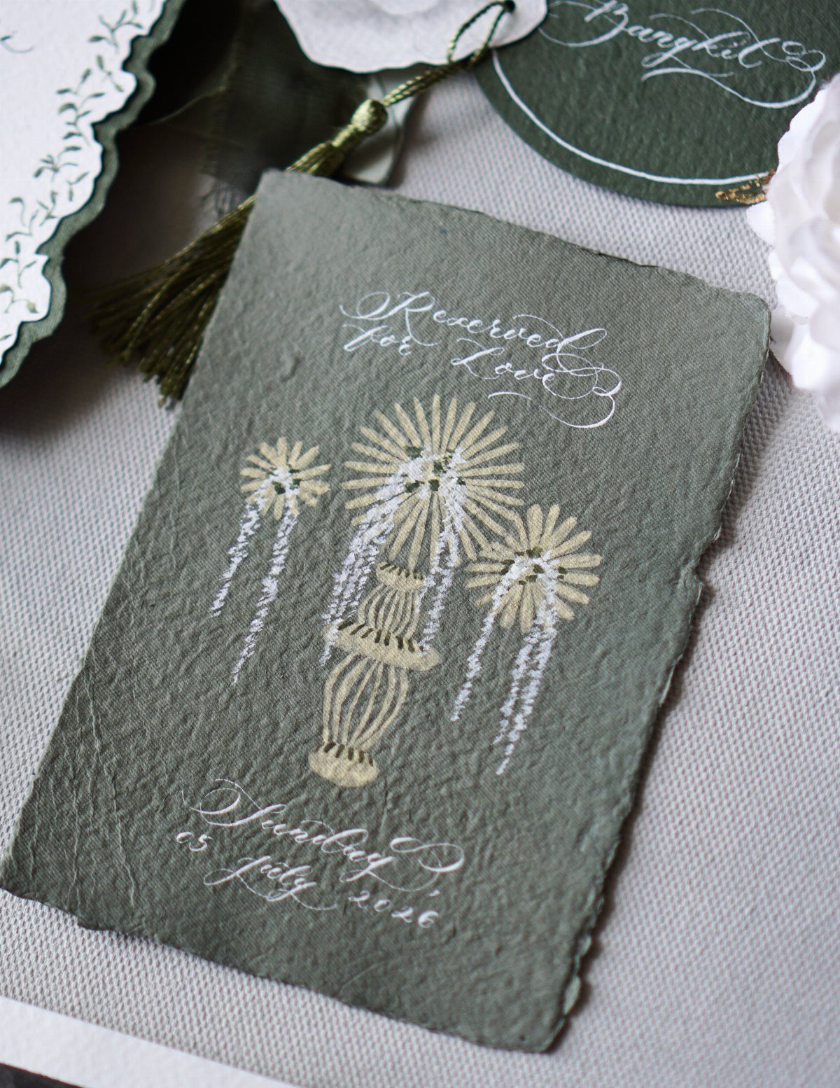 Sage green wedding invitation card featuring a gold monstrance illustration and white calligraphy.