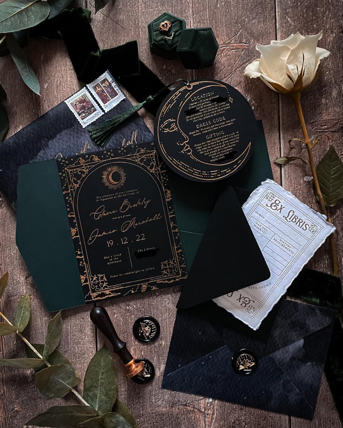 Celestial wedding invitation suite with dark green envelopes, gold star details, and white rose.