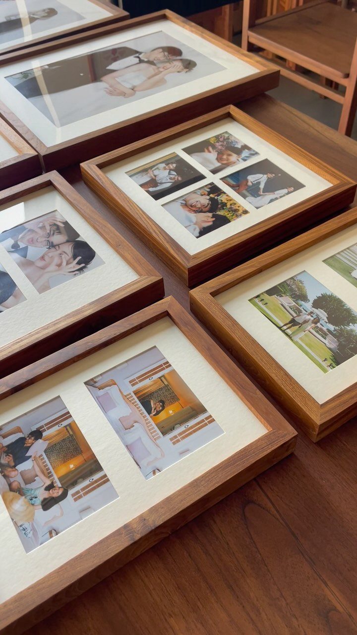 Wooden picture frames containing wedding photos arranged on a dark brown wooden table.