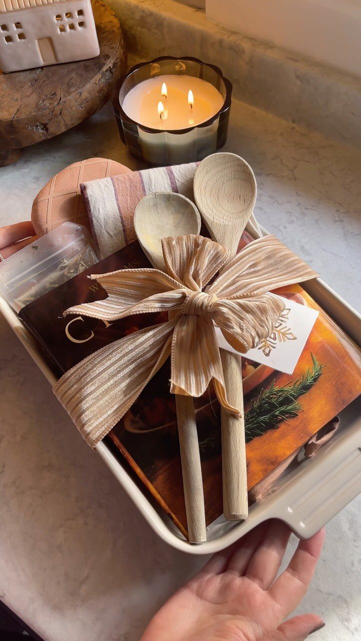 Gift tray with a cookbook, wooden spoons tied with ribbon, and a candle.