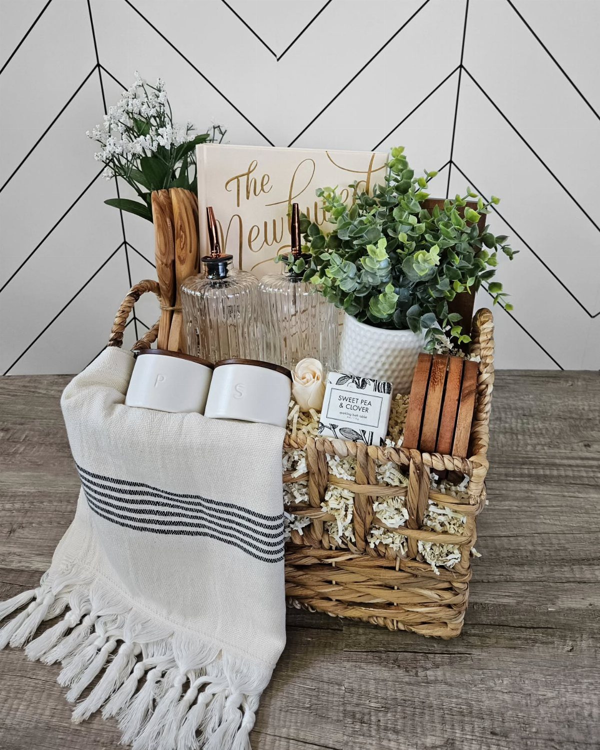 Woven wicker gift basket with a white blanket, candles, and a potted plant.