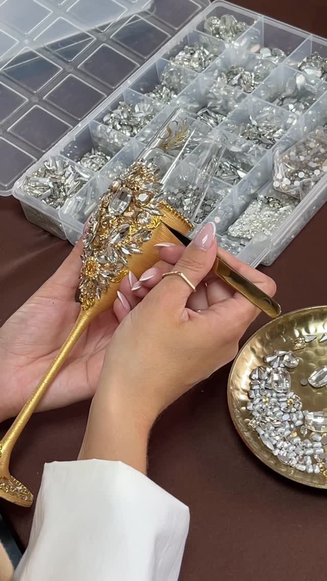 Hands decorating a gold champagne glass with sparkling rhinestones and crystals