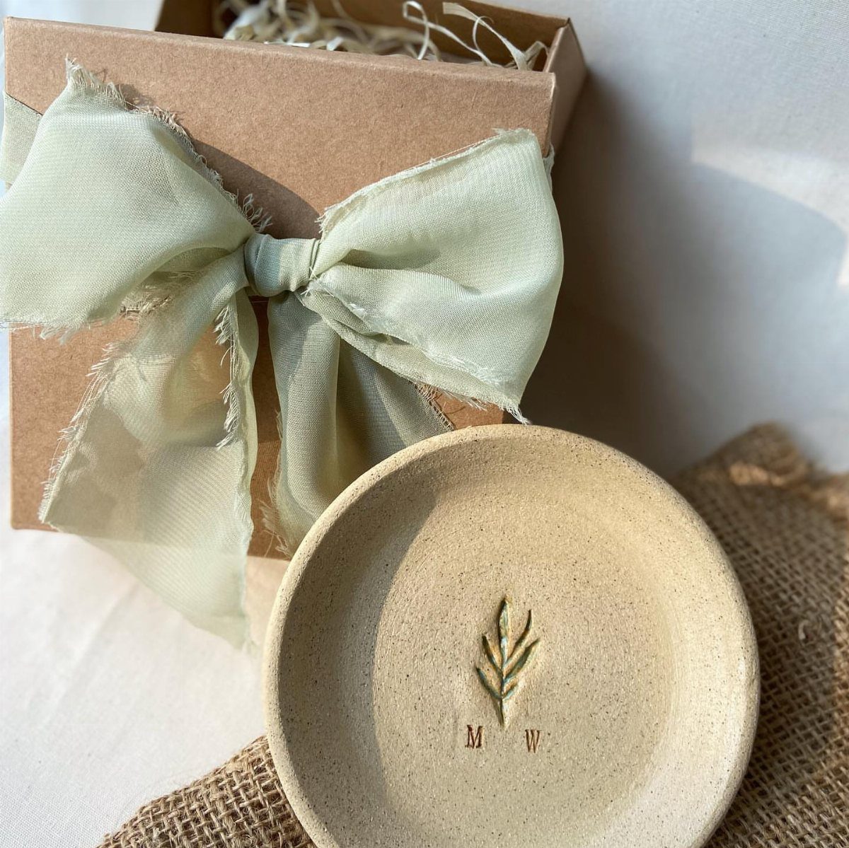 Beige ceramic bowl with leaf design and initials next to a gift box