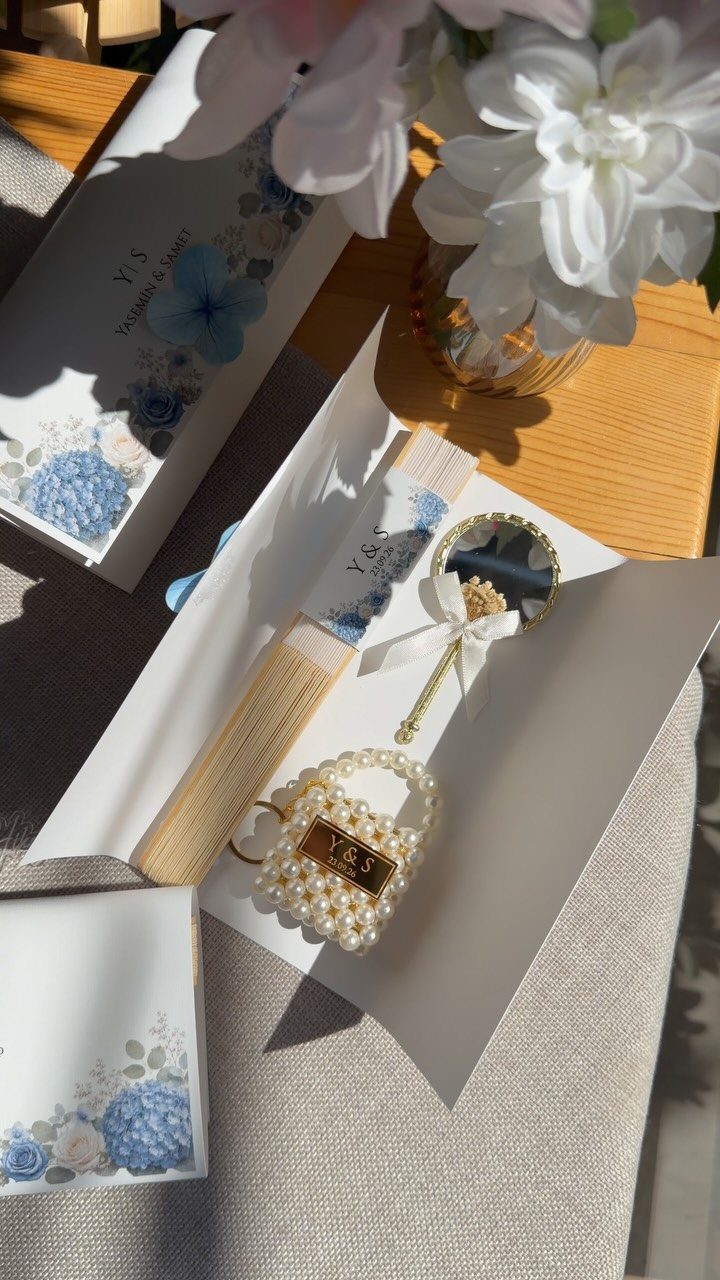Pearl-beaded handbag charm with gold initials on white wedding stationery and flowers.