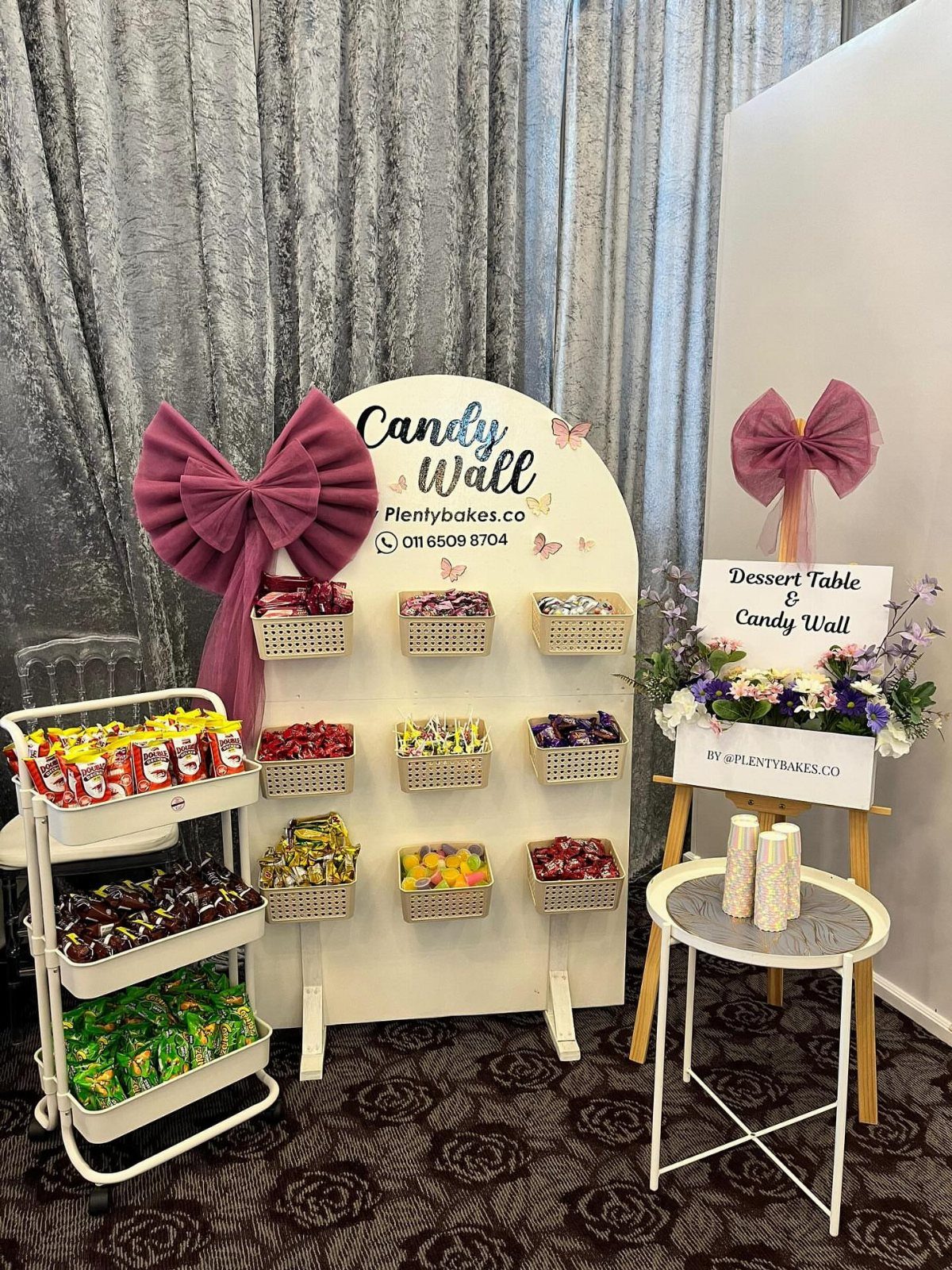 Candy wall display with baskets of sweets, a tiered cart, and purple bows.