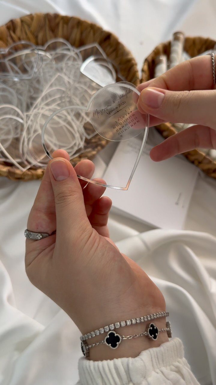 Heart-shaped clear acrylic plaques with engraving held by hands over a woven basket.