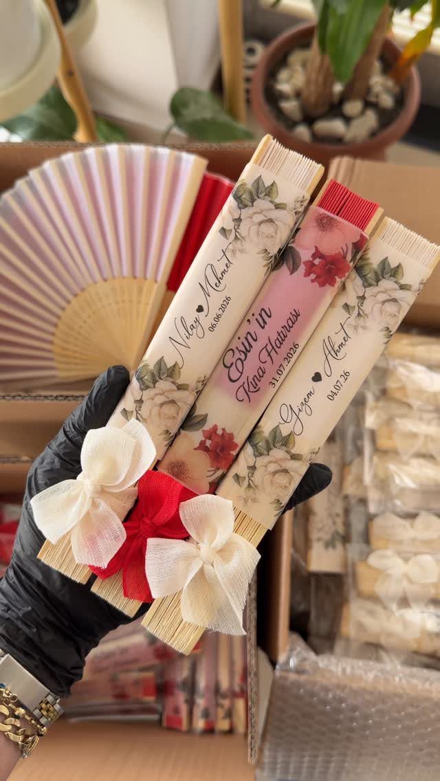 Decorative folding fans with floral prints and bows held by a gloved hand.