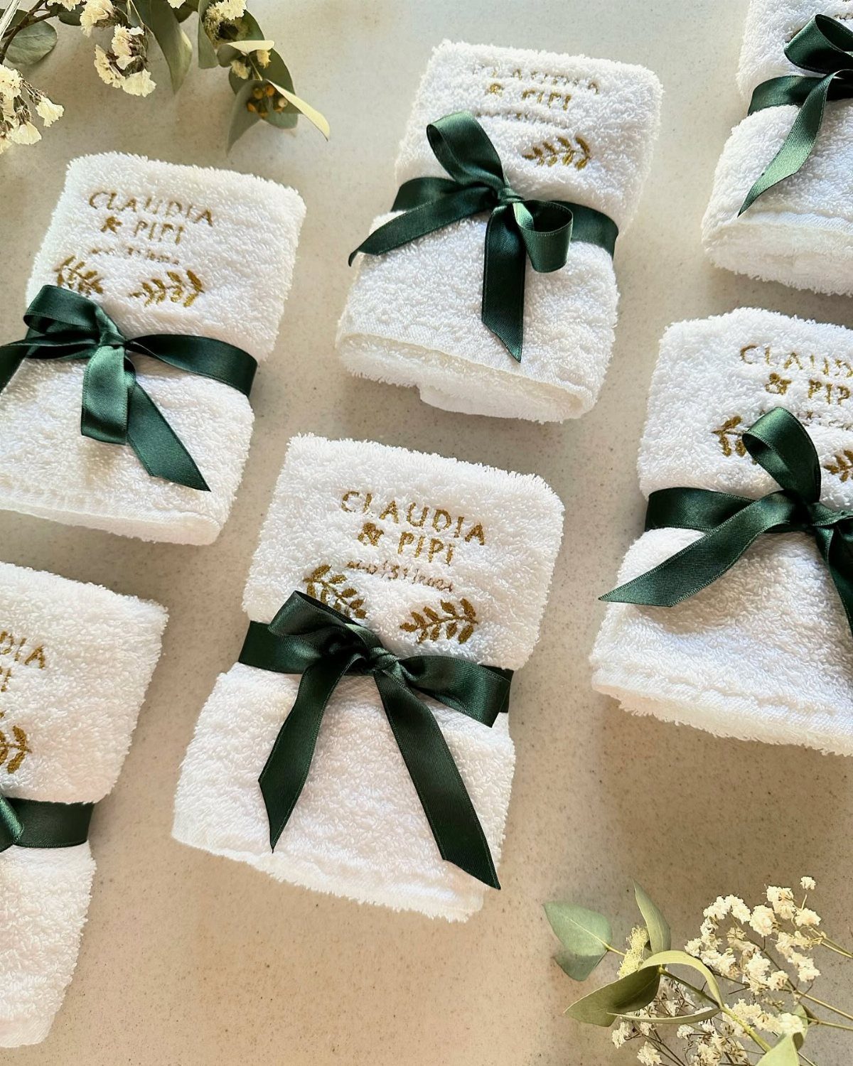 White rolled towels with gold embroidery and green ribbons for wedding favors.