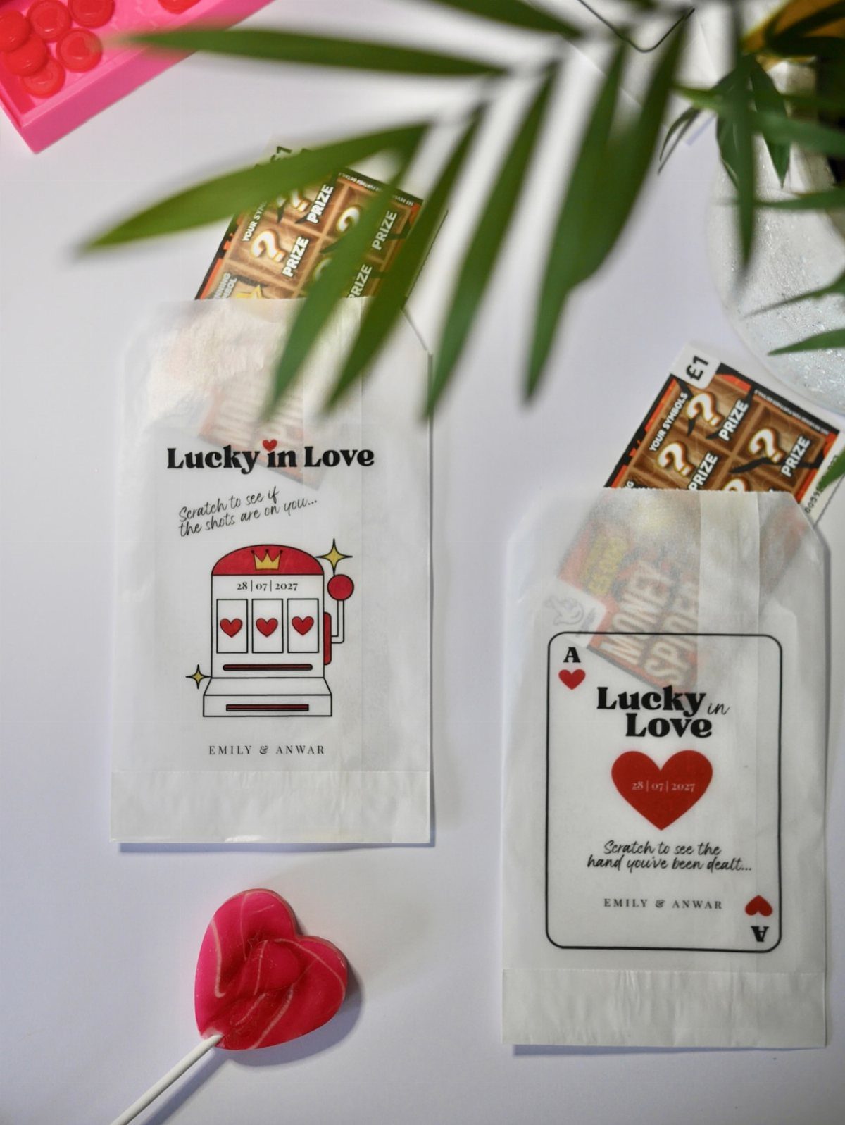 White favor bags containing scratch-off lottery tickets with heart-shaped lollipop and green leaves.