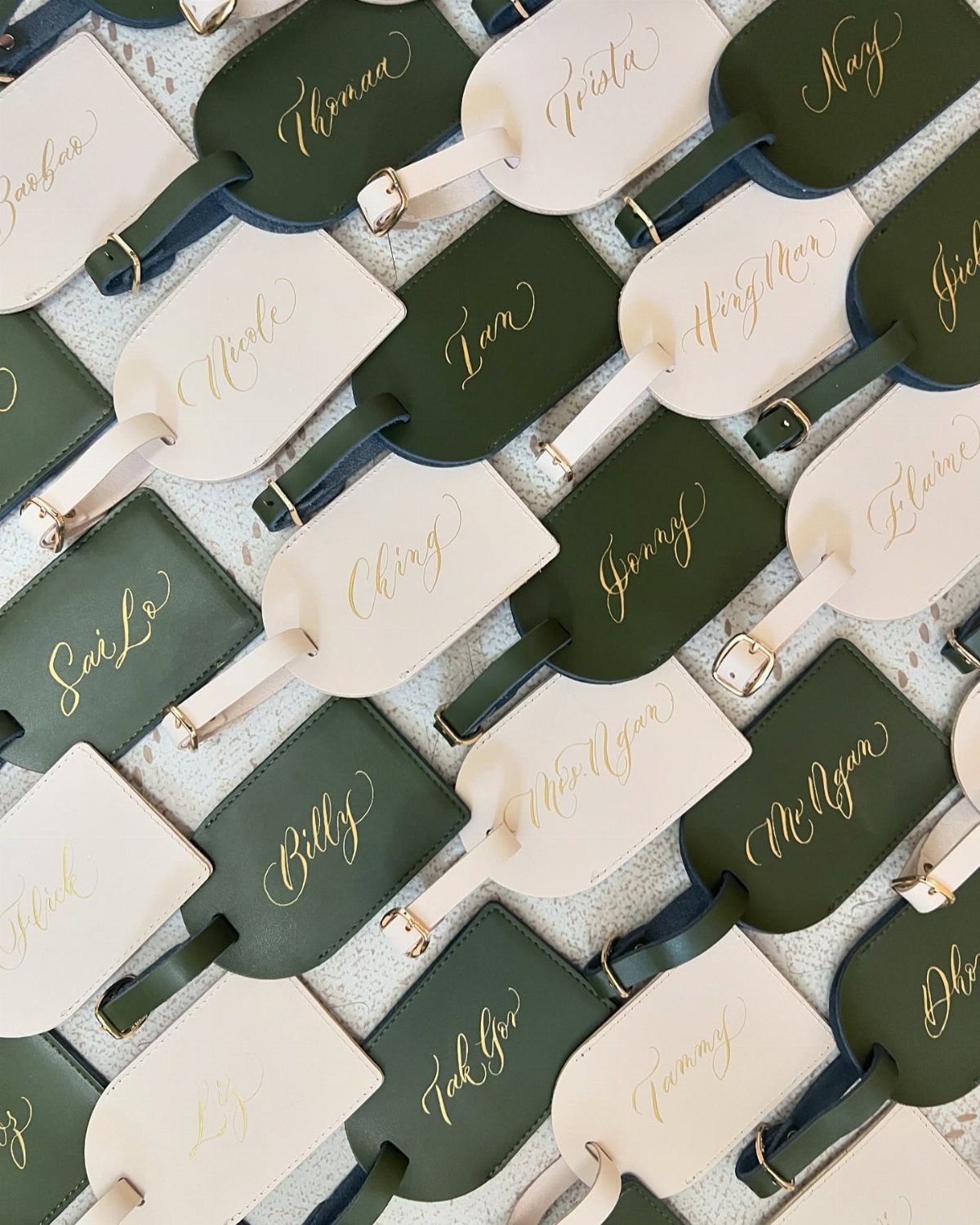 Leather luggage tags in green and cream with gold calligraphic names on white fabric.