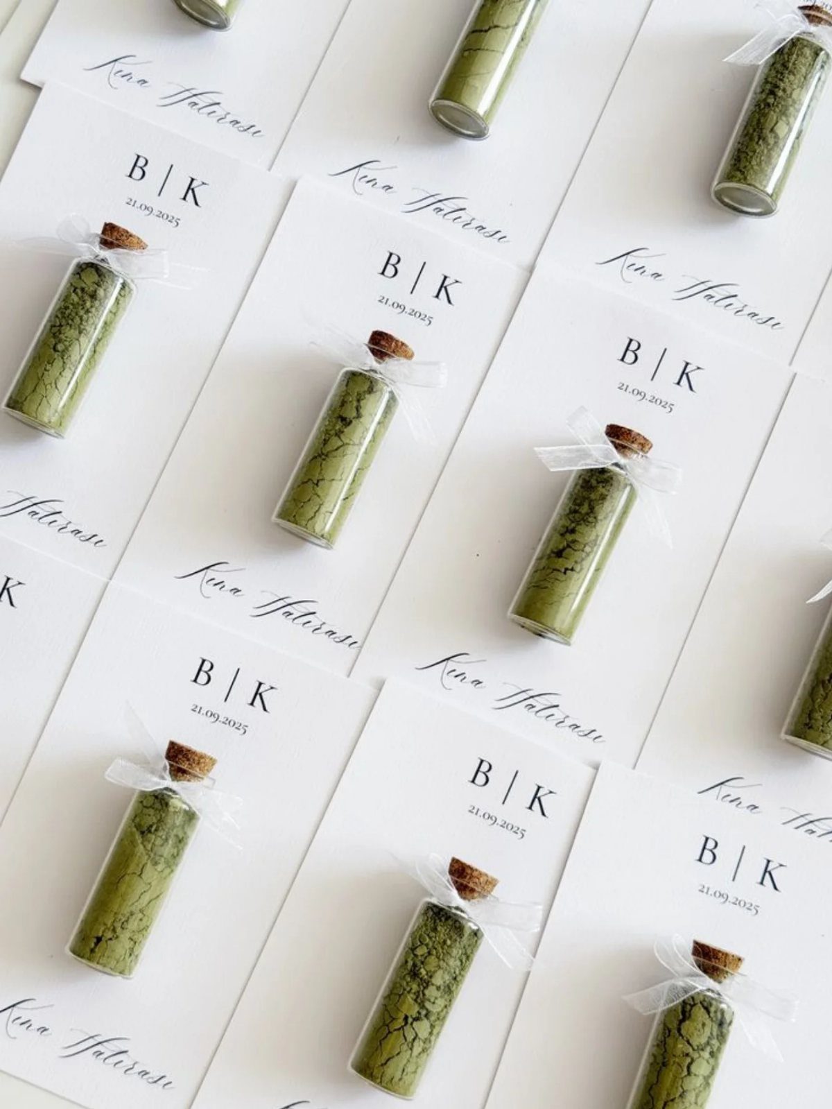 Small glass vials with green powder and white ribbons on personalized white cards.