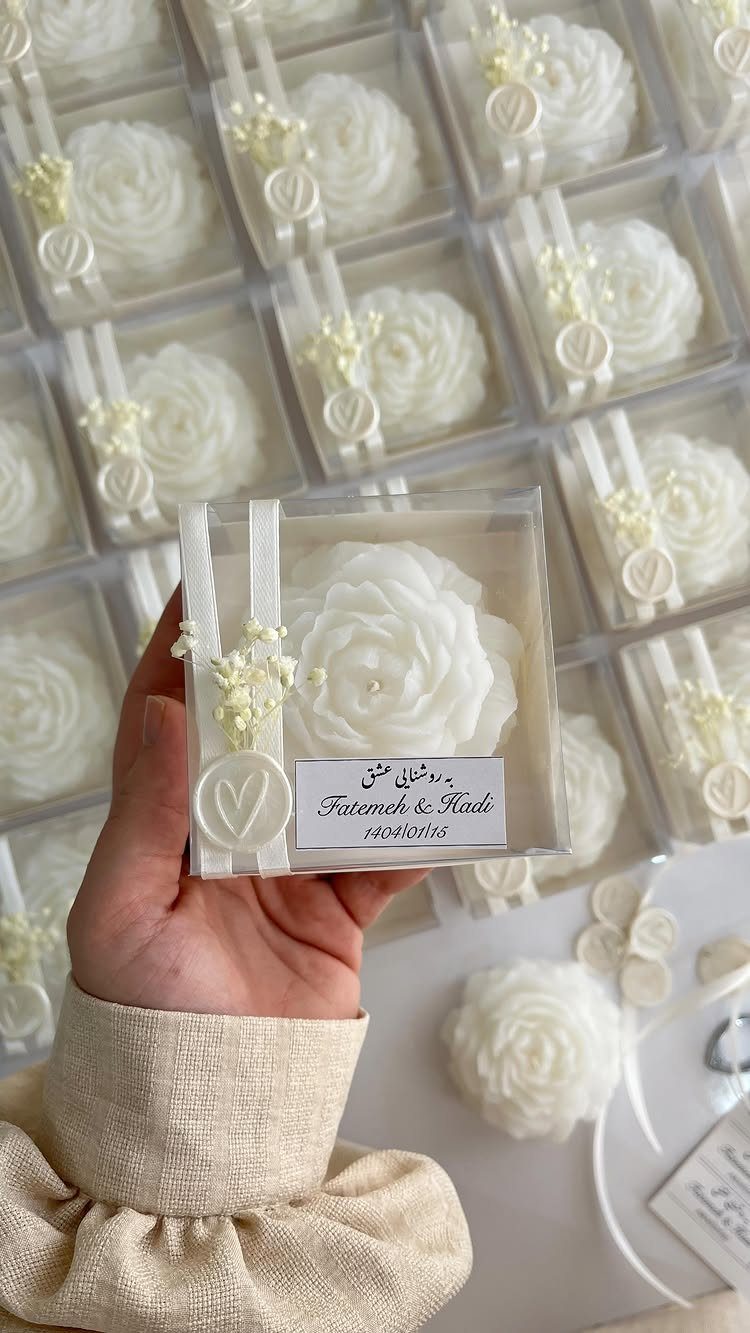 White rose-shaped candle in a clear gift box with a personalized name tag.