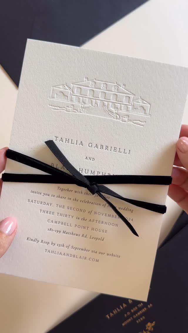 White wedding invitation with black text and a black ribbon bow tied around it