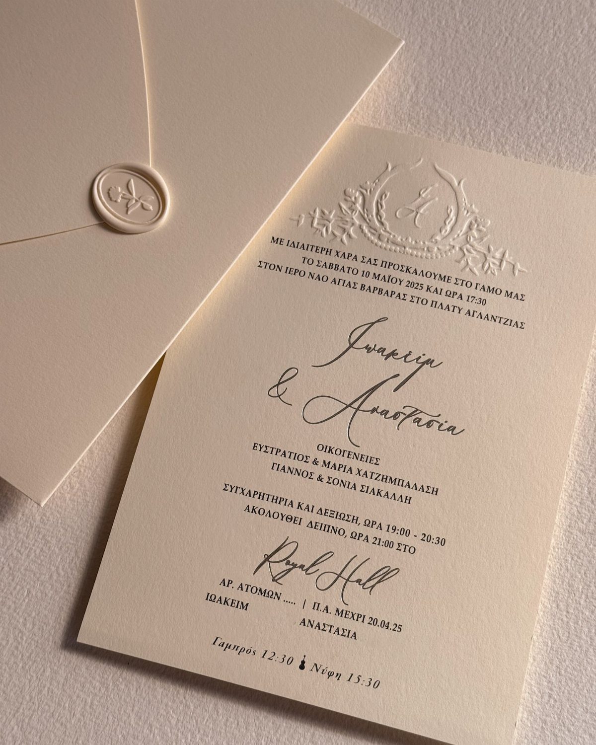 Cream wedding invitation with Greek text and an embossed crest beside a wax-sealed envelope.