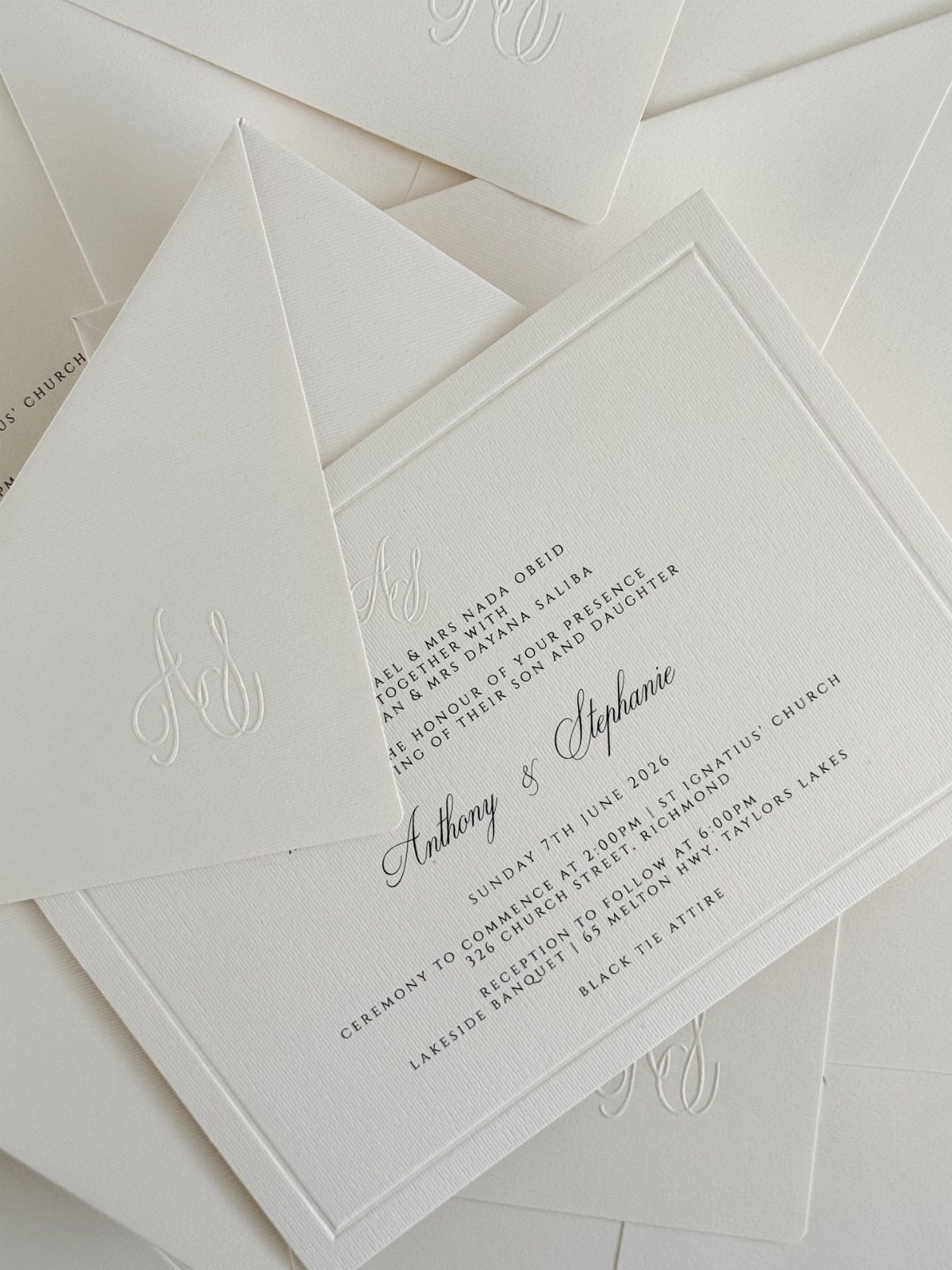 White wedding invitation cards with black text and embossed monogram envelopes.