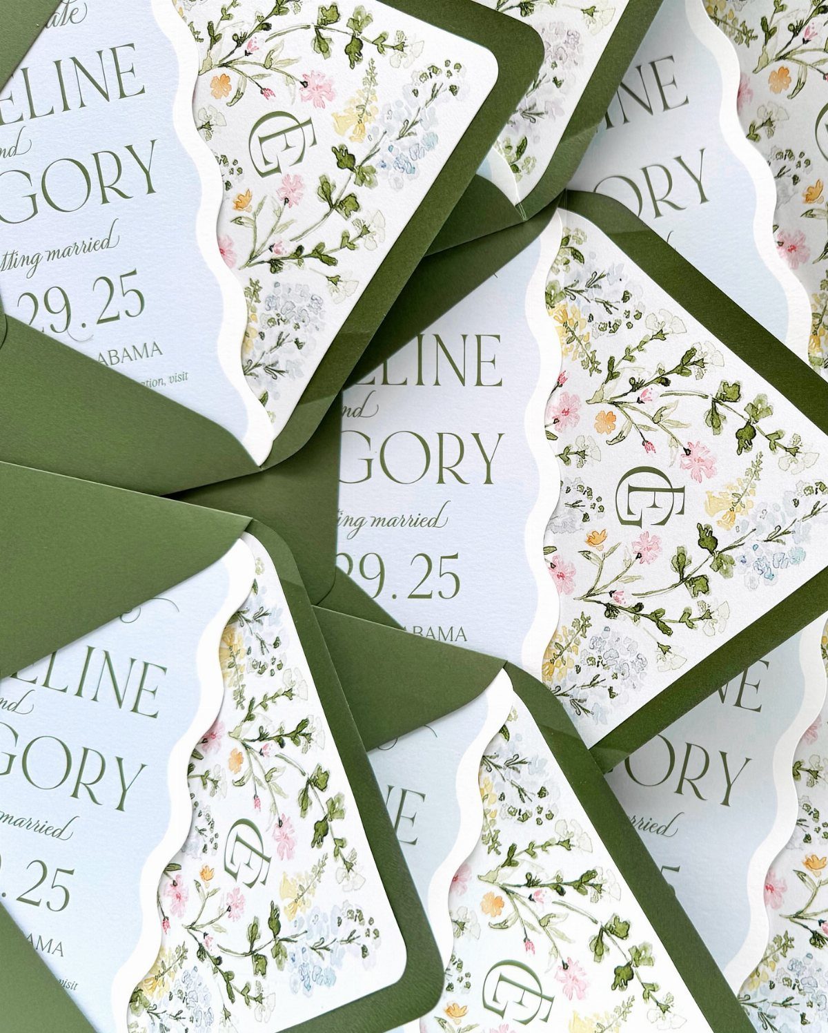 Floral wedding invitations with green leaf motifs tucked into olive green envelopes.