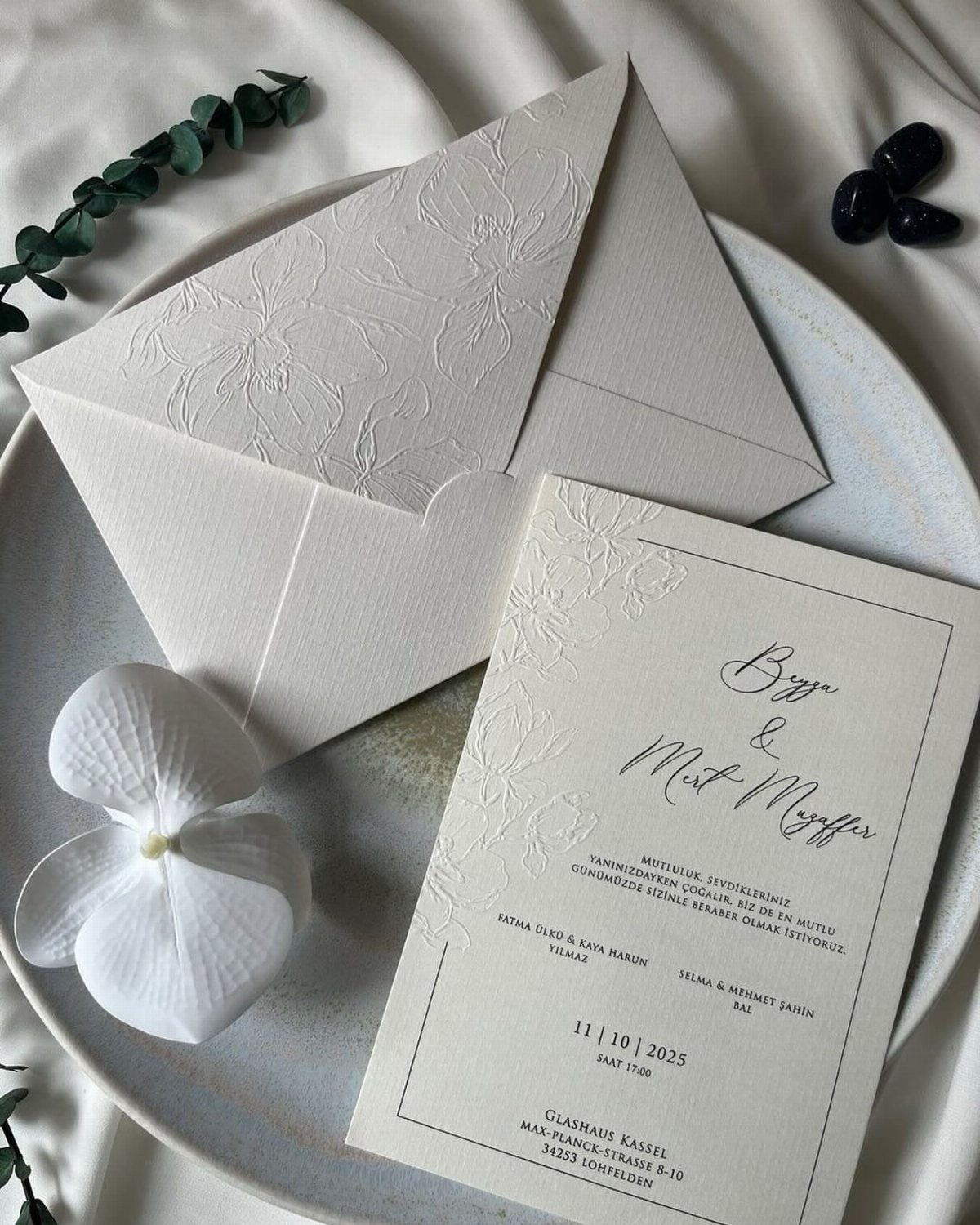 Ivory wedding invitation and envelope with embossed floral liner on a white plate.
