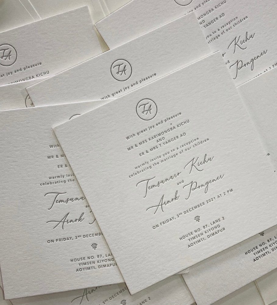 White square wedding invitations with debossed grey text and a circular monogram.