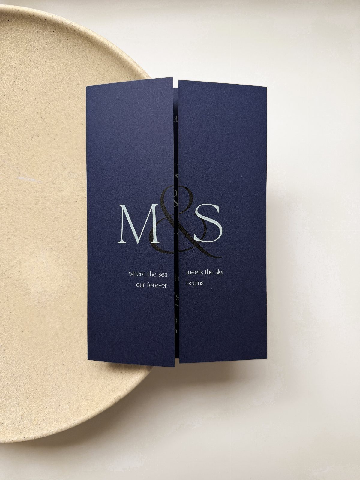 Navy blue wedding invitation with white serif lettering resting on a beige plate.