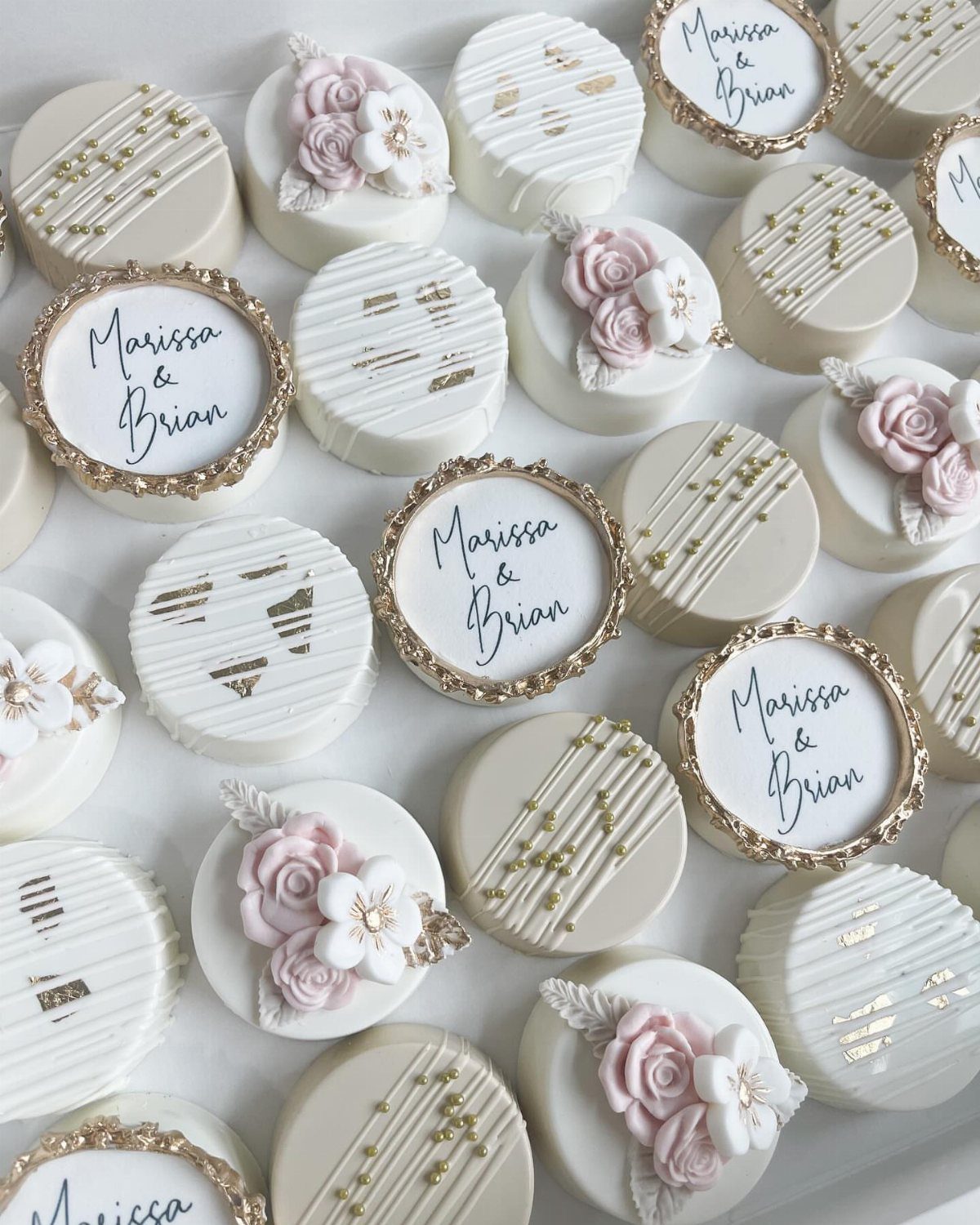 White chocolate covered Oreos decorated with pink roses, gold accents, and personalized names.