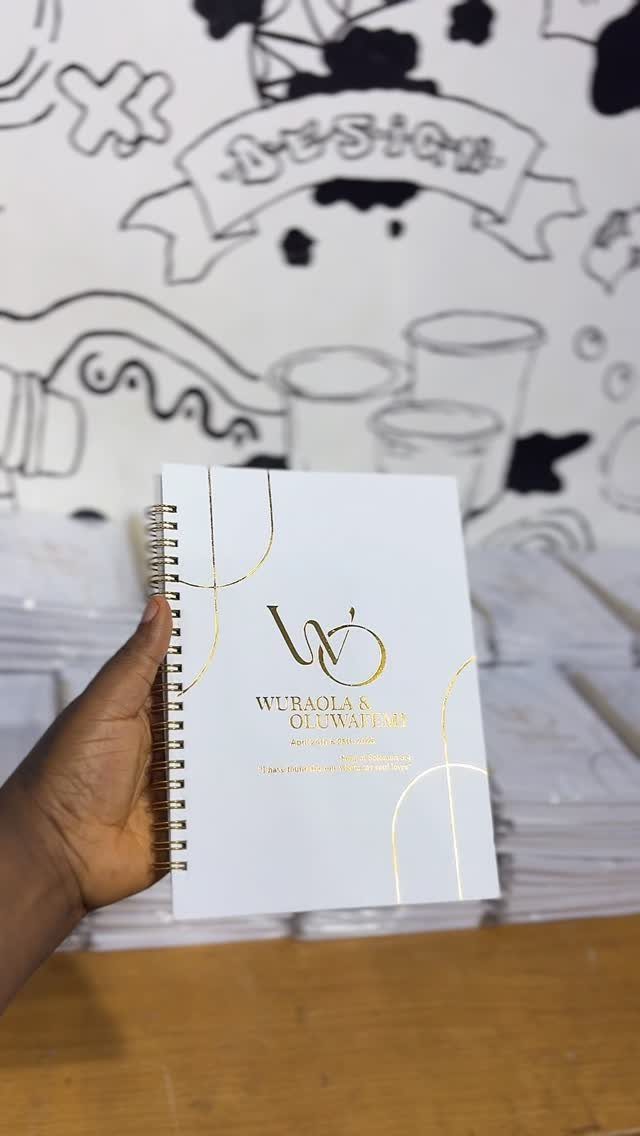 White spiral notepad with gold foil lettering held by a hand against art background
